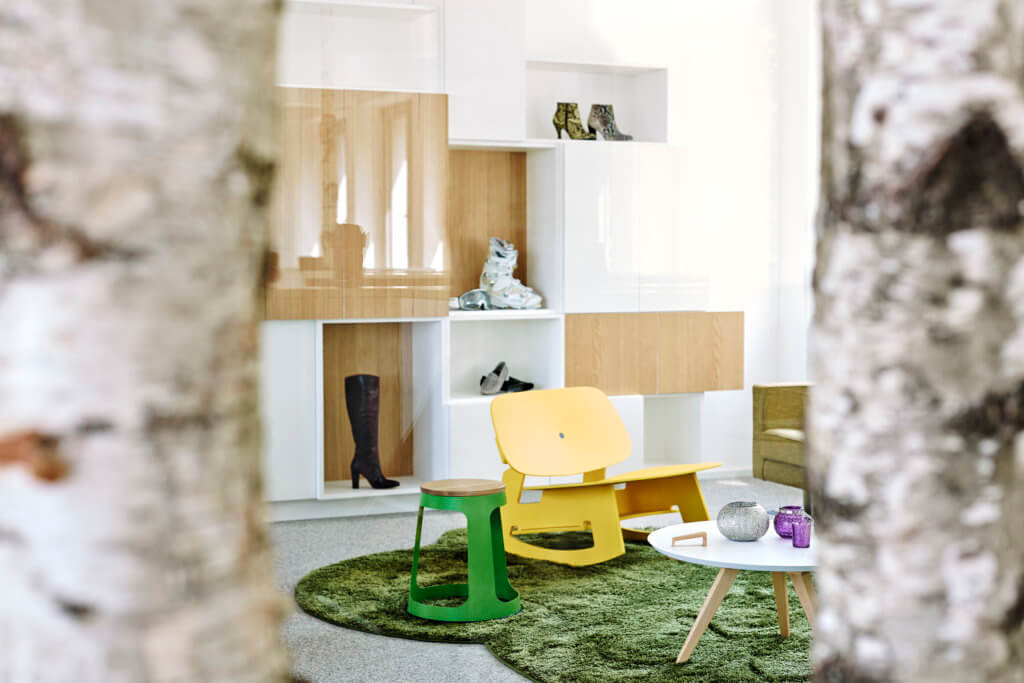 Wandregale aus Eichenholz und weißem MDF. Davor ein gelber Schaukelstuhl an grünem Tisch in den Büroräumen der Hansmann PR Agentur. Interior Design von camp.