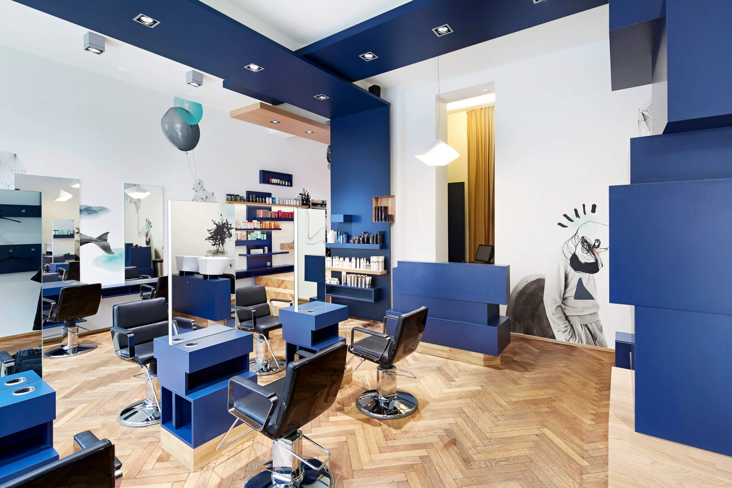 Das Bild zeigt den Innenraum des Friseursalons New Hair in München. Dunkelblaues Möbliar und affällige Wandgrafiken bilden einen optischen Blickfang.