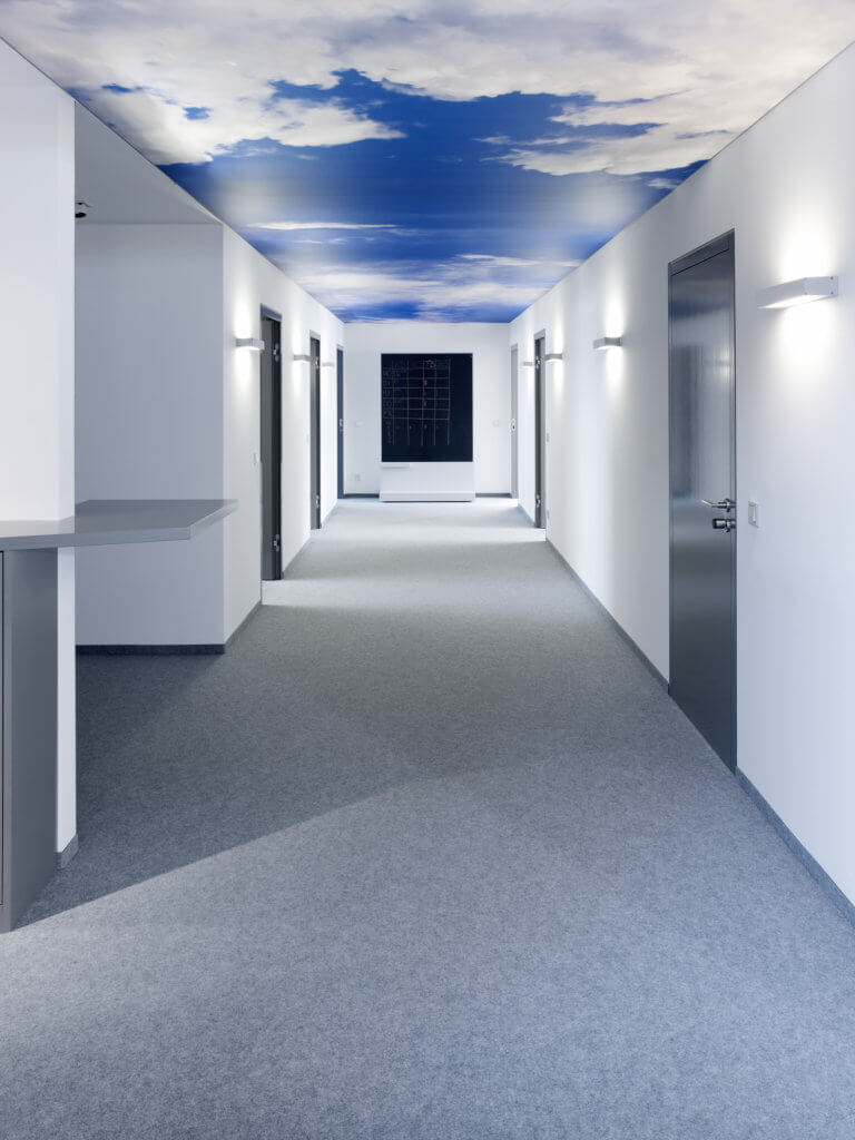 Flurbereich Büro Schleich und Habler Immobilien-Consulting mit grauem Teppich und Wolkenfotografie als Deckenverkleidung.