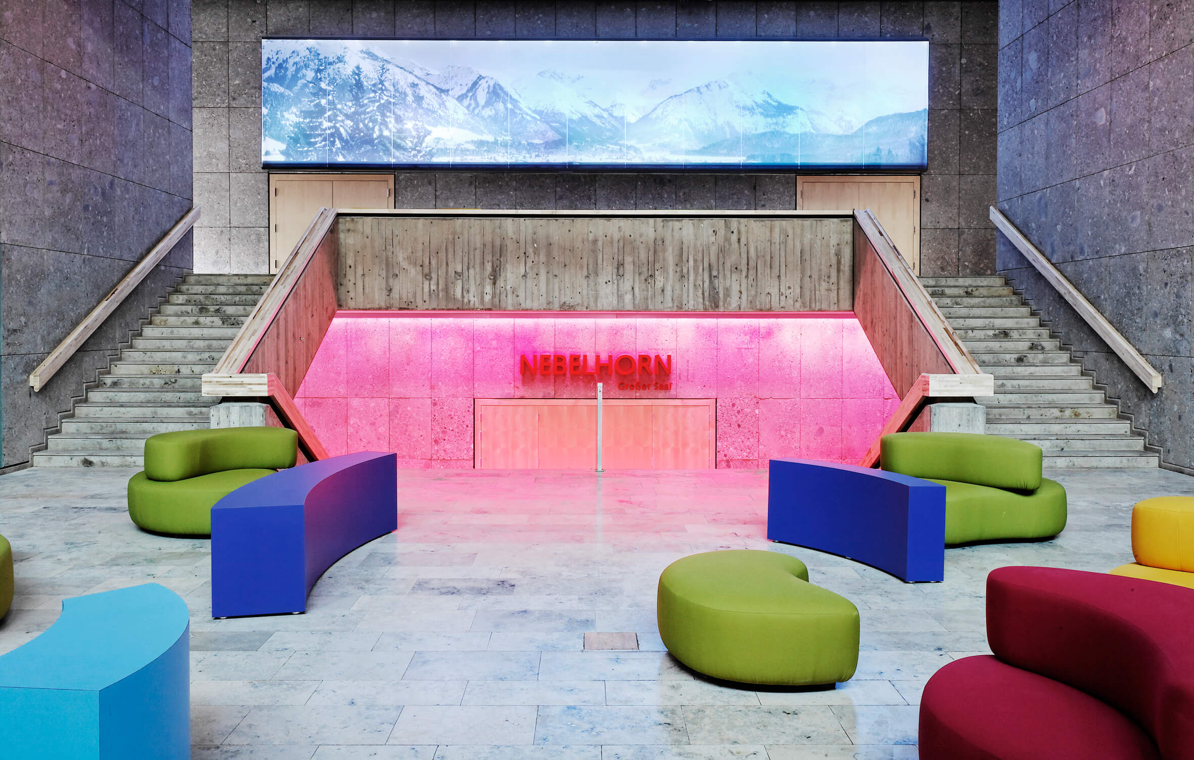 Eingangsbereich des neuen Kurhauses in Oberstdorf mit farbigen Sesseln und einem raumgebenden Wandbild mit Bergpanorama.