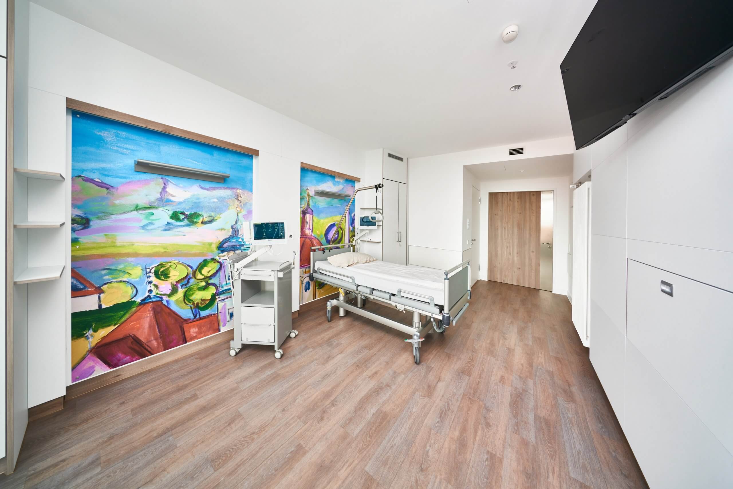 Das Bild zeigt ein Patientenzimmer in der Klinik Ottobeuren im Allgäu. Die Wände sind mit großen Werken regionaler Künstler gestaltet.