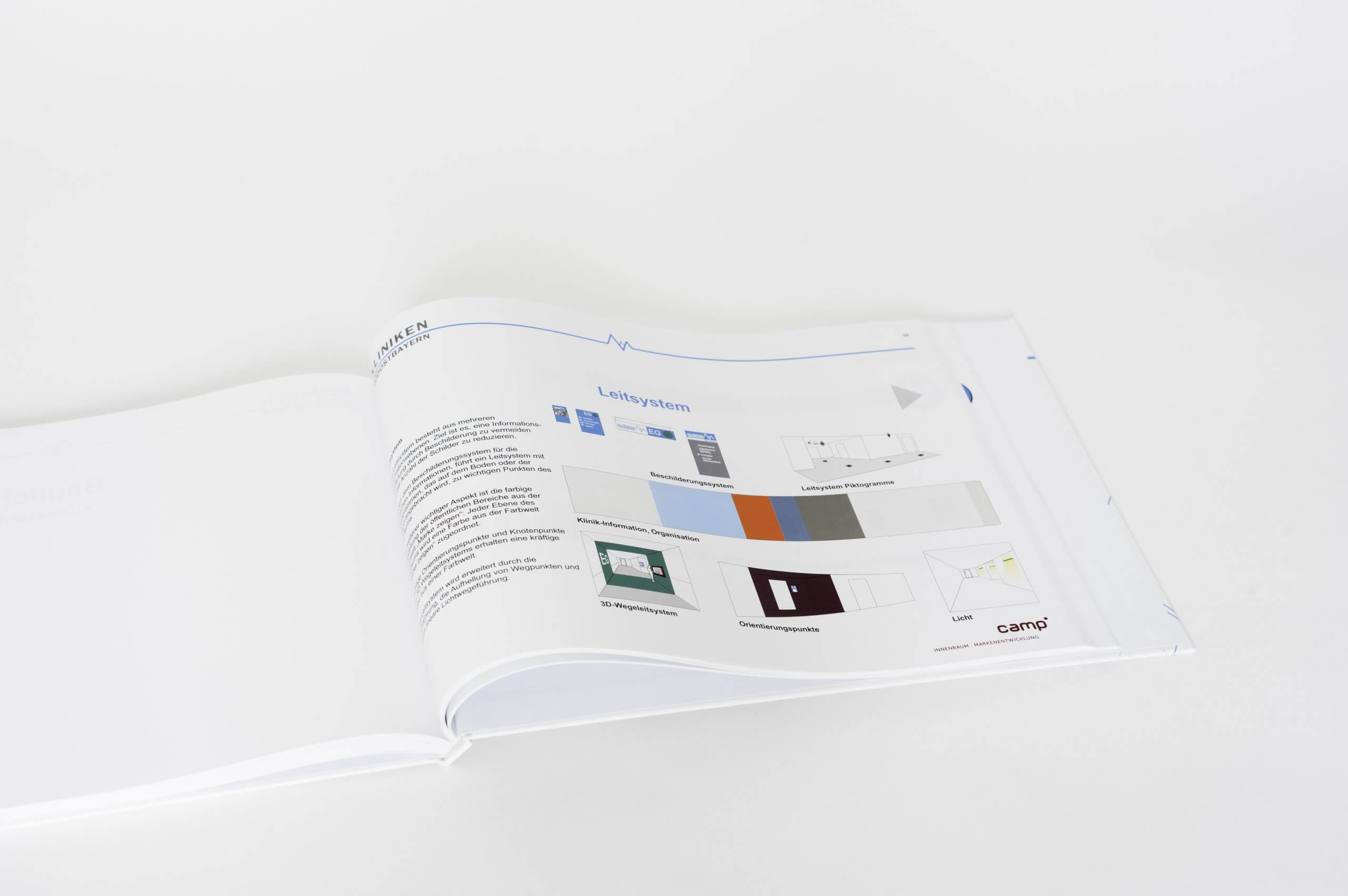 Das Markenhandbuch mit einer aufgeschlagenen Seite. Sie zeigt die architektonischen Grundlagen zum Wegeleitsystem der Kliniken Südostbayern.